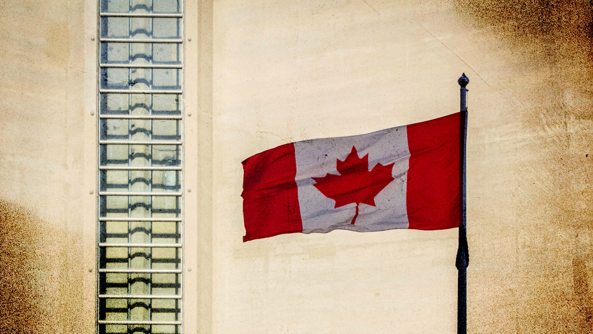 Canadian flag waving in front of a beige building with modern glass windows