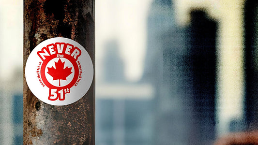 Close-up of a Never the 51st sticker on a weathered metal post, with a blurred city skyline in the background